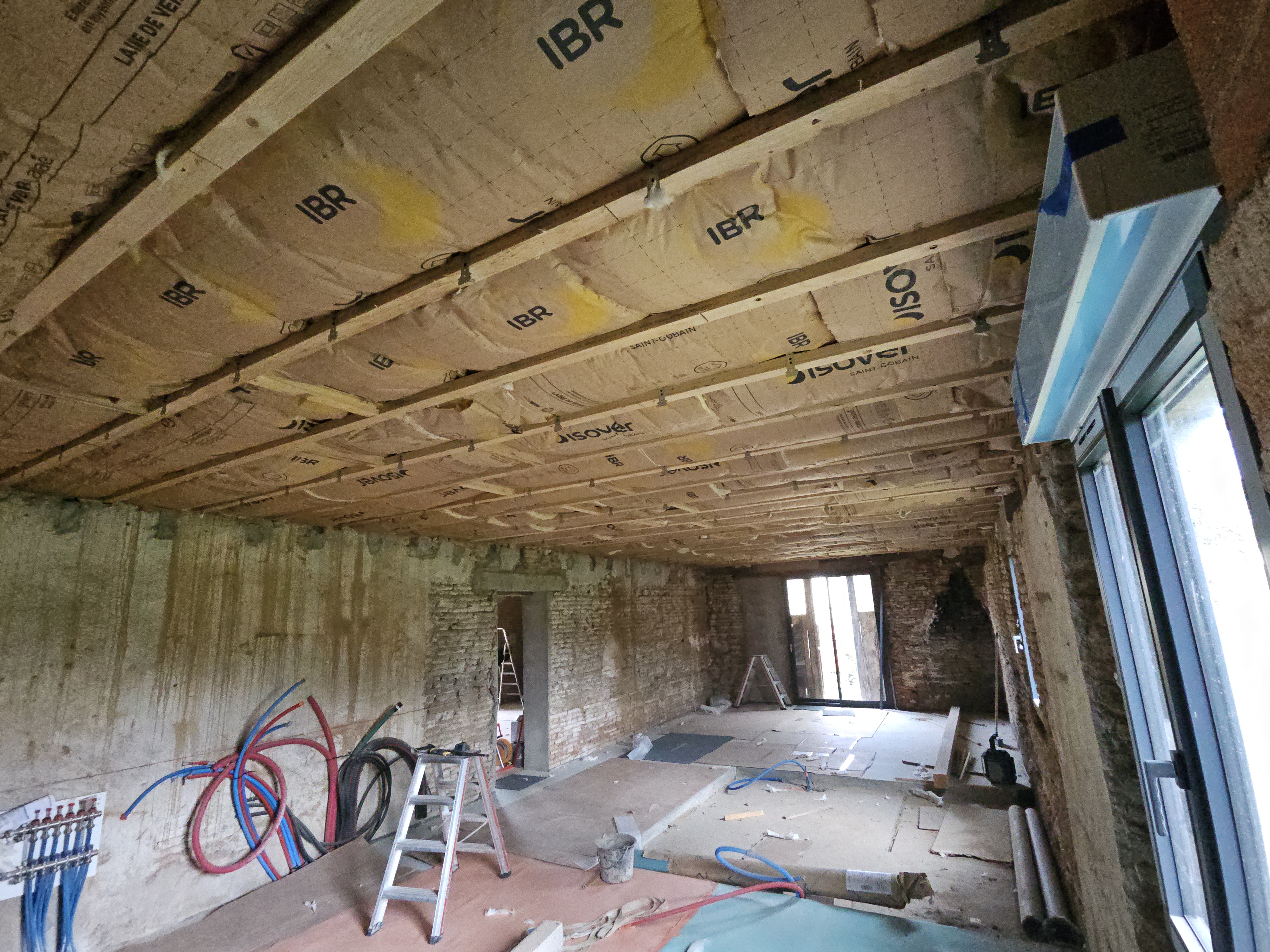 Isolation thermique d'un plafond entre solives en bois avec des rouleaux de laine de verre Isover IBR, dans un chantier de rénovation de maison ancienne par l'EURL Teulières